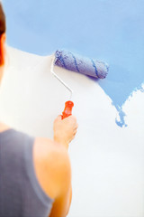 Young woman painting wall with roller brush.