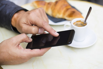 Man using a mobile phone on cafe terrace, croissant and coffee