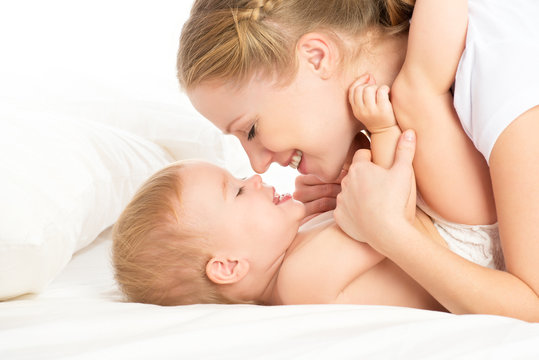 Happy Family Mother And Baby Having Fun Playing, Laughing On Bed