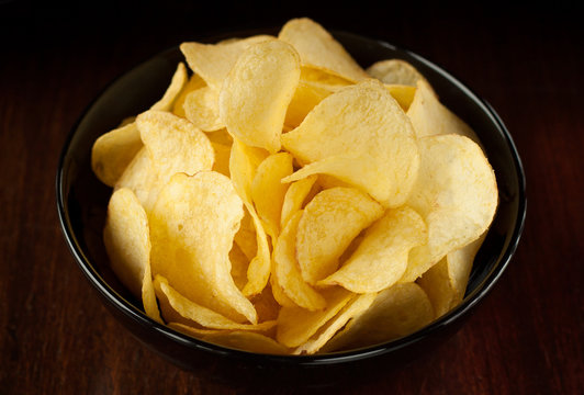Potato chips in black bowl on dark background - snack bar