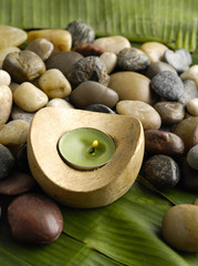Fototapeta na wymiar candle in wooden bowl and pebbles on banana leaf