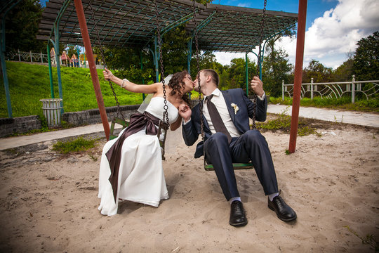 Young groom and bride kissing on swing at playground