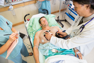 Doctor Defibrillating Male Patient In Hospital - obrazy, fototapety, plakaty