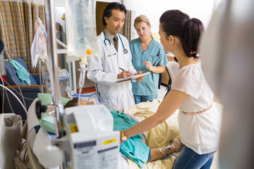 Woman Standing By Patient's Bed Looking At Doctor And Nurse