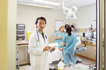 Doctor Holding Digital Tablet With Nurses Examining Patient