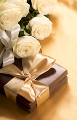 Bouquet of beautiful roses next to a gift on a gold table