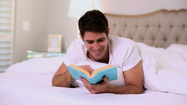 Happy handsome man reading in bed