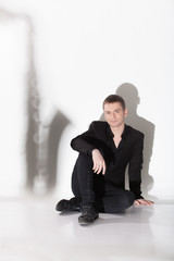 man in black suit sitting on floor against shadow of saxophone