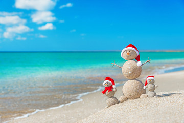 Snowmans family at sea beach in santa hat. New years and christm