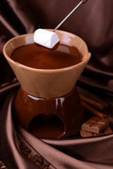 Chocolate fondue with marshmallow candies, on brown background
