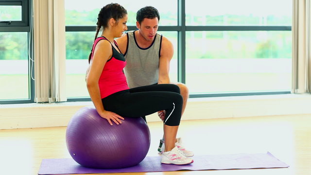 Pretty woman training sitting on fitness ball with coach