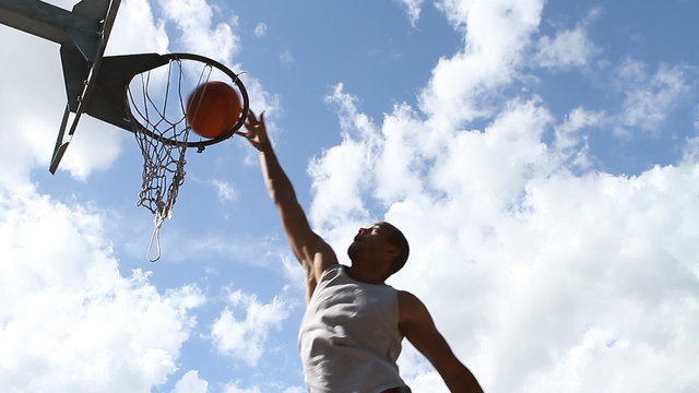 Basketball player slam dunking against a cloudy sky