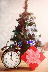 Alarm clock and gift box at xmas tree background