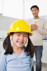Cute girl in yellow hard hat with father in background