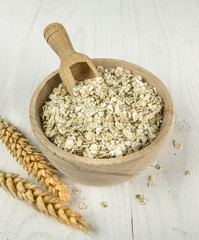 Wooden bowl and scoop with oatmeal flakes on wooden table