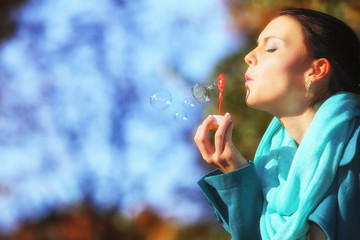 Woman having fun blowing bubbles in autumnal park