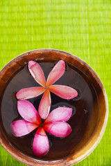 Two frangipani flower in wooden bowl on straw mat
