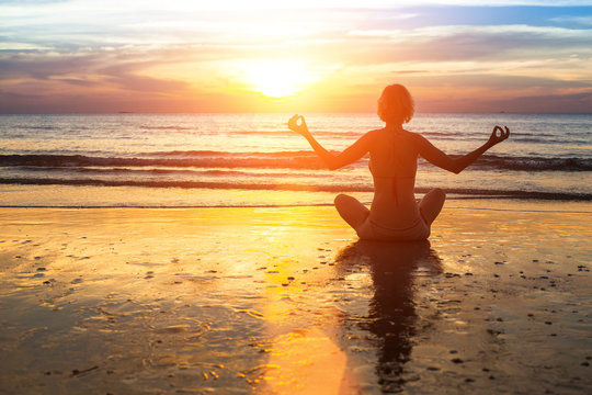 Silhouette of woman practicing yoga on the beach during sunset.