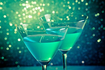 glasses of blue cocktail on dark green tint light bokeh