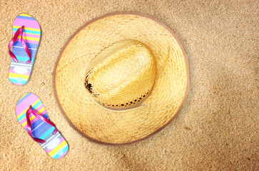 Fototapeta na wymiar top view of straw hat and flip flops on beach sand