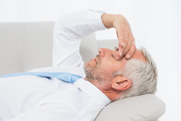 Fototapeta premium Tired mature businessman resting on sofa in living room
