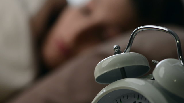 A young woman is woken by her alarm clock
