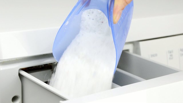 hand pouring detergent into the washing machine