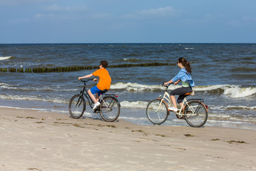 Fototapeta premium Teenage girl and boy biking on beach