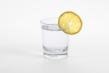Glass with water and piece of a lemon on a white background