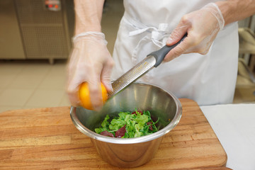 Chef is zesting orange in bowl with salad