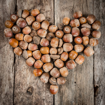 Acorns forming a heart on a wooden background