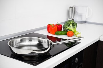 Frying pan and vegetables in modern with induction stove - obrazy, fototapety, plakaty