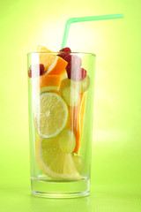transparent glass with citrus fruits, on green background