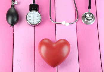 Tonometer, stethoscope and heart on wooden table close-up