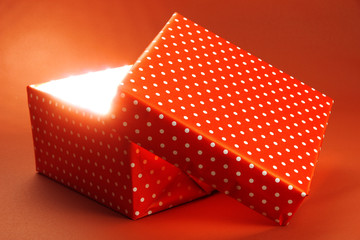 Gift box with bright light on it on red background