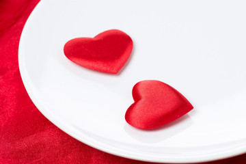 Two silk heart on a plate on red background, selective focus