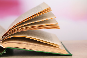 Opened book on wooden table on bright background