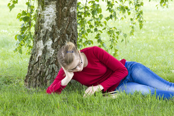 Young girl reading book in park in spring day