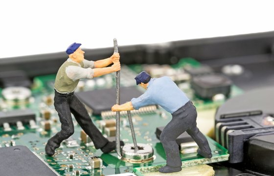 Miniature engineers repairing a computer hard drive