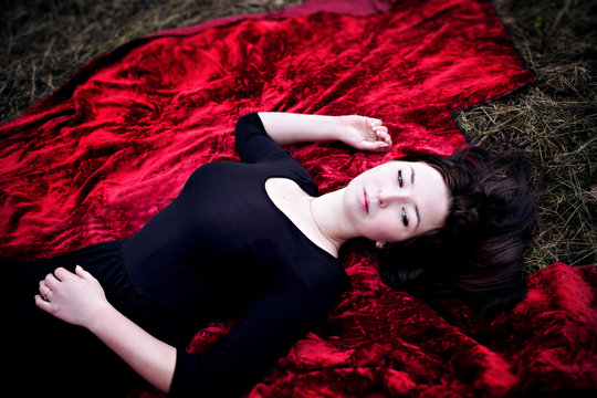 Pale woman in black dress lying on red carpet