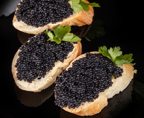 Small sandwiches with black caviar on dark plate