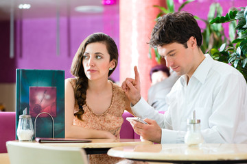 Young couple in cafe not interacting but on phone
