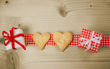 Herzen und Geschenke auf rotem Geschenkband vor Holzhintergrund