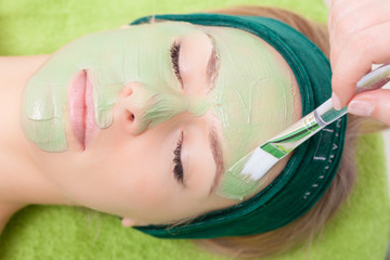 Beauty salon. Cosmetician applying facial mask at woman face.