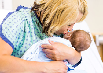 Obraz na płótnie Canvas Mother Kissing Newborn Babygirl In Hospital