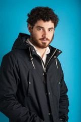 Portrait of confident young man wearing winter jacket against bl