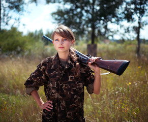 Young beautiful girl with a shotgun looks into the distance