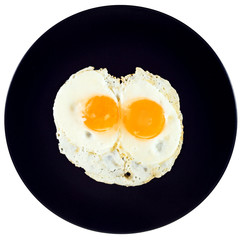 top view of two fried eggs on ceramic black plate
