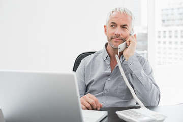 Businessman on call in front of laptop at office desk