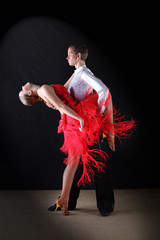 Latino dancers in ballroom against on black